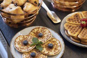 A variety of breakfast items including pancakes, waffles, and pastries on plates and in a basket.