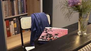 Una estantería con libros, un sillón con una chaqueta y un jarrón con flores sobre una mesa.