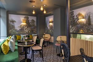 A cozy lounge area with a green sofa, multiple chairs, and tables. There are wall murals depicting nature scenes.