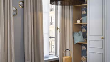 Un dormitorio con cama, una ventana con cortinas, una cesta de mimbre y una repisa con objetos decorativos.