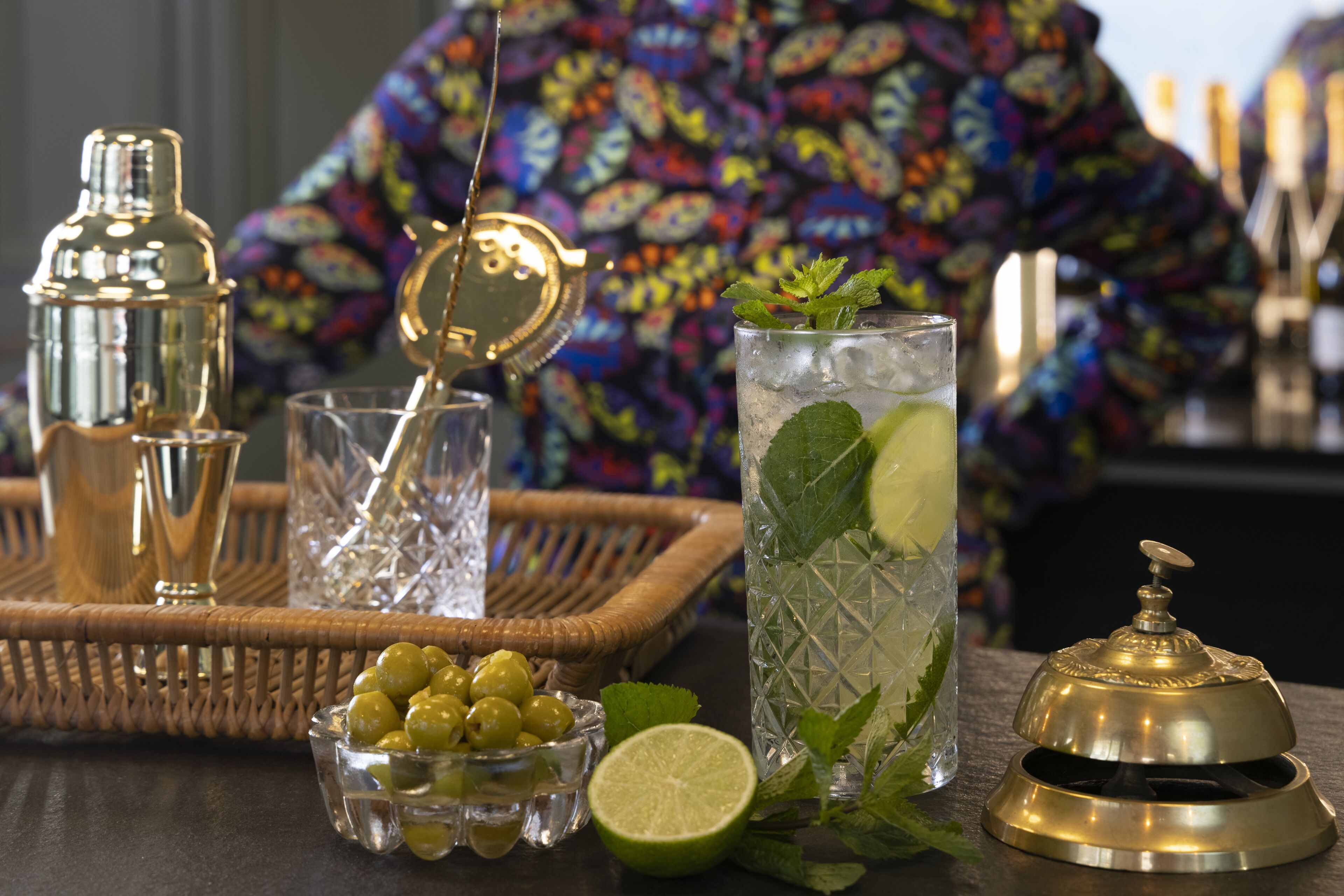 A bar setting with a cocktail glass, a bottle, a bowl of olives, and a lime.