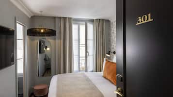 Habitación de hotel con cama, espejo, televisión, puerta con el número 301 y ventana con cortinas.