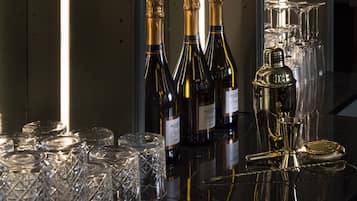 Una zona de bar con varias botellas de vino, copas de vino y un decantador dorado sobre una superficie reflectante.