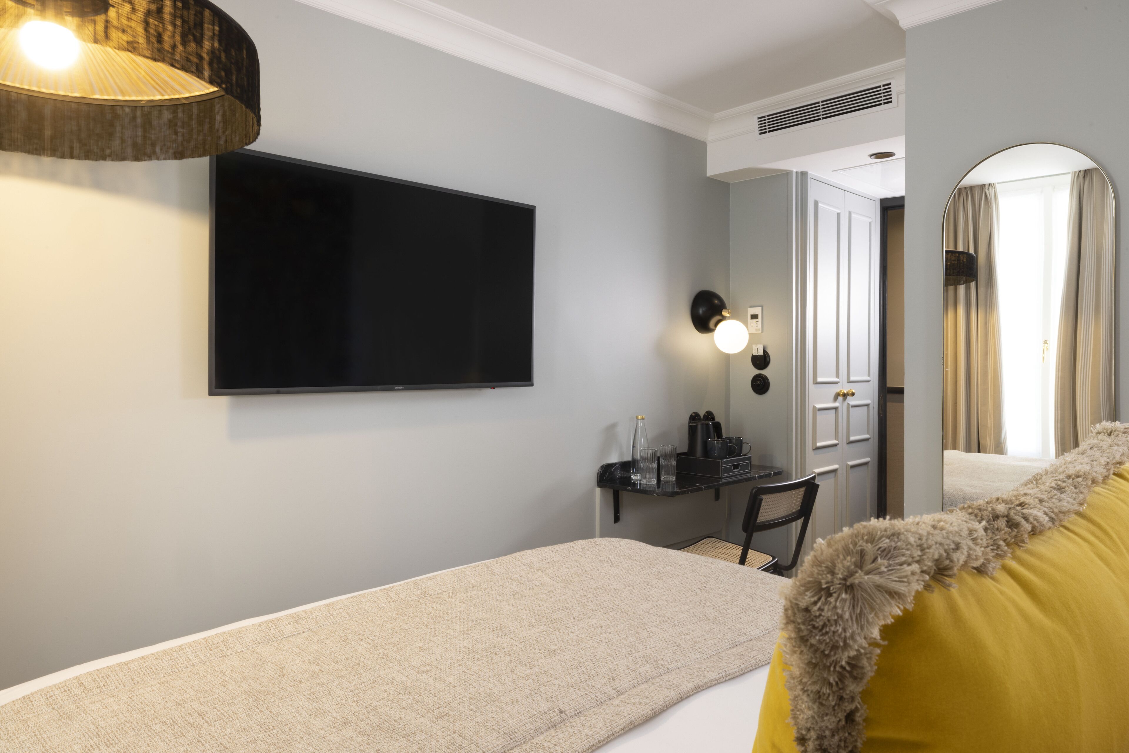 A modern hotel room with a flat-screen TV mounted on the wall, a desk with a chair, and a bed with a fluffy pillow.
