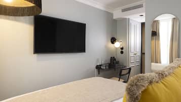 A modern hotel room with a flat-screen TV mounted on the wall, a desk with a chair, and a bed with a fluffy pillow.