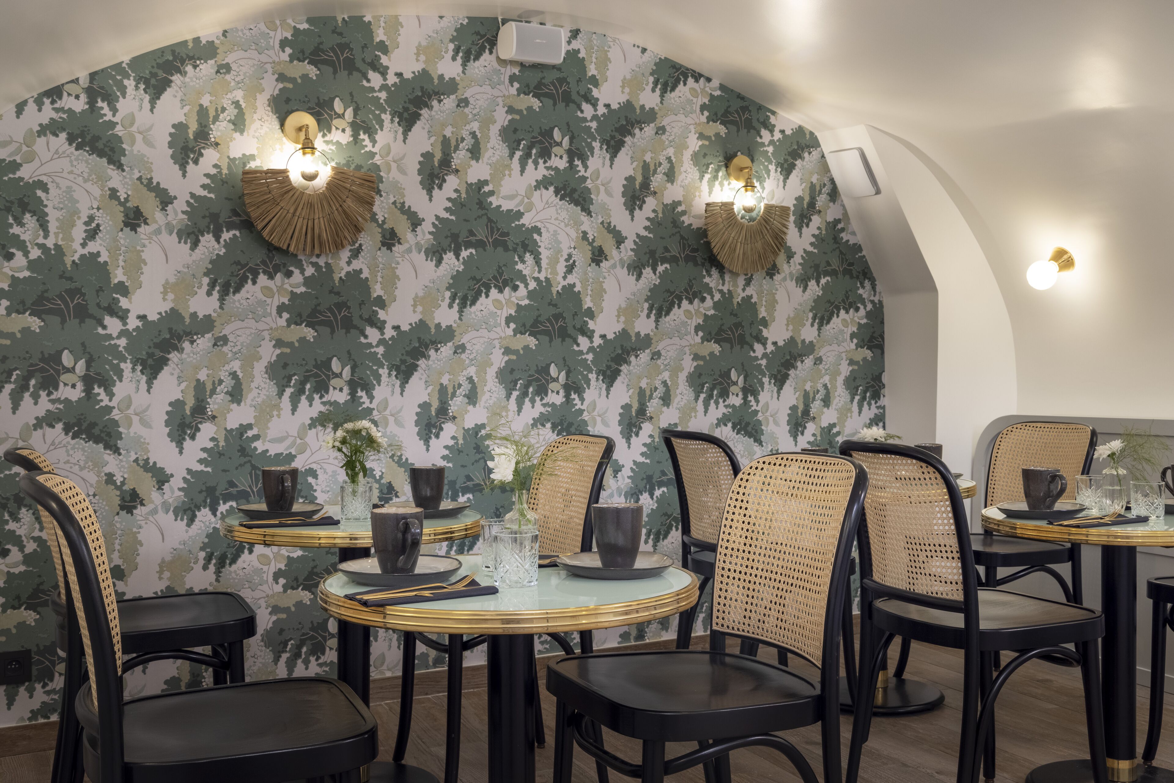 A dining area with round tables, black chairs, and wall-mounted light fixtures.