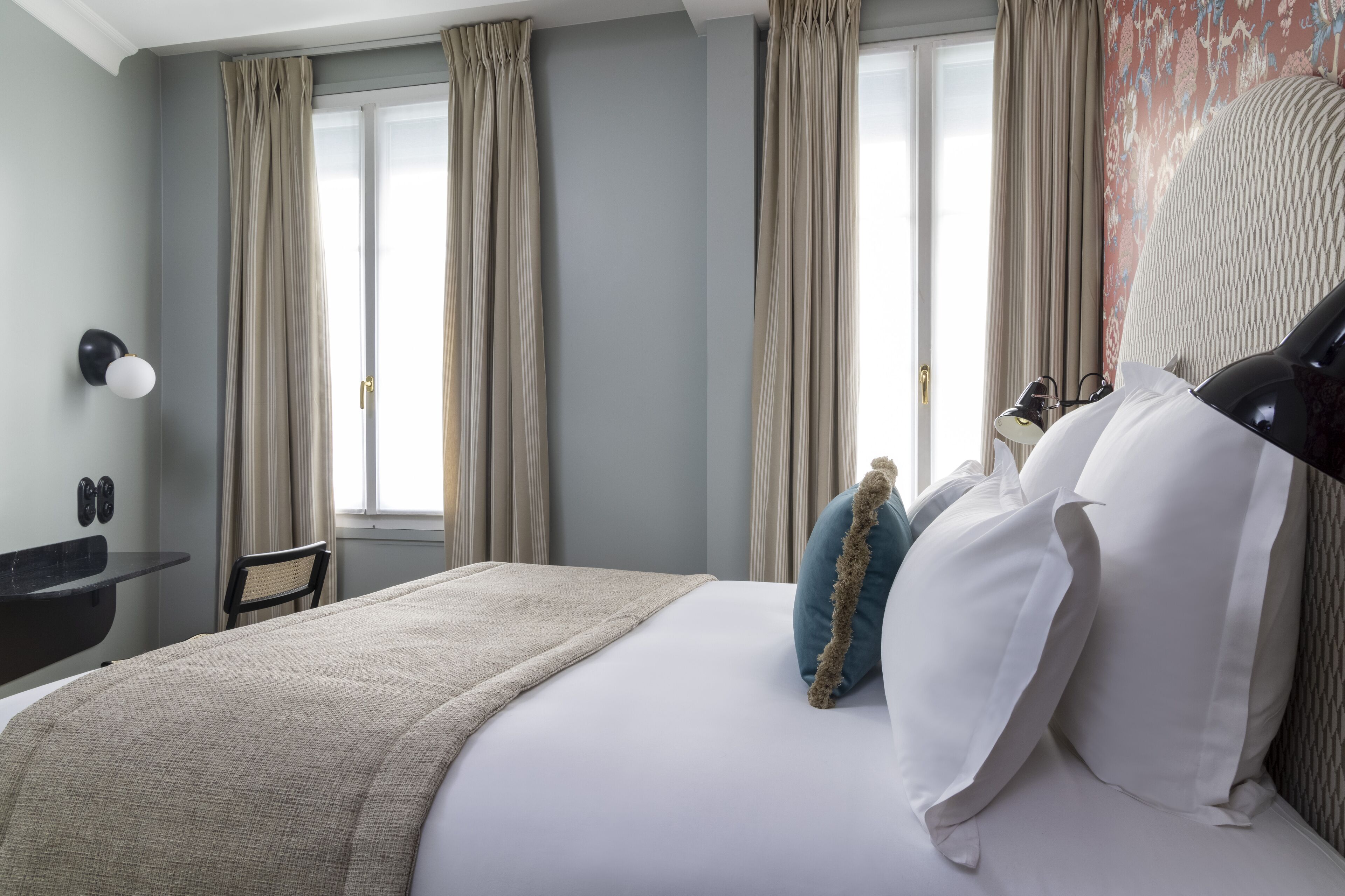 Een hotelkamer met een bed, nachtkastje, lamp en raam met gordijnen.