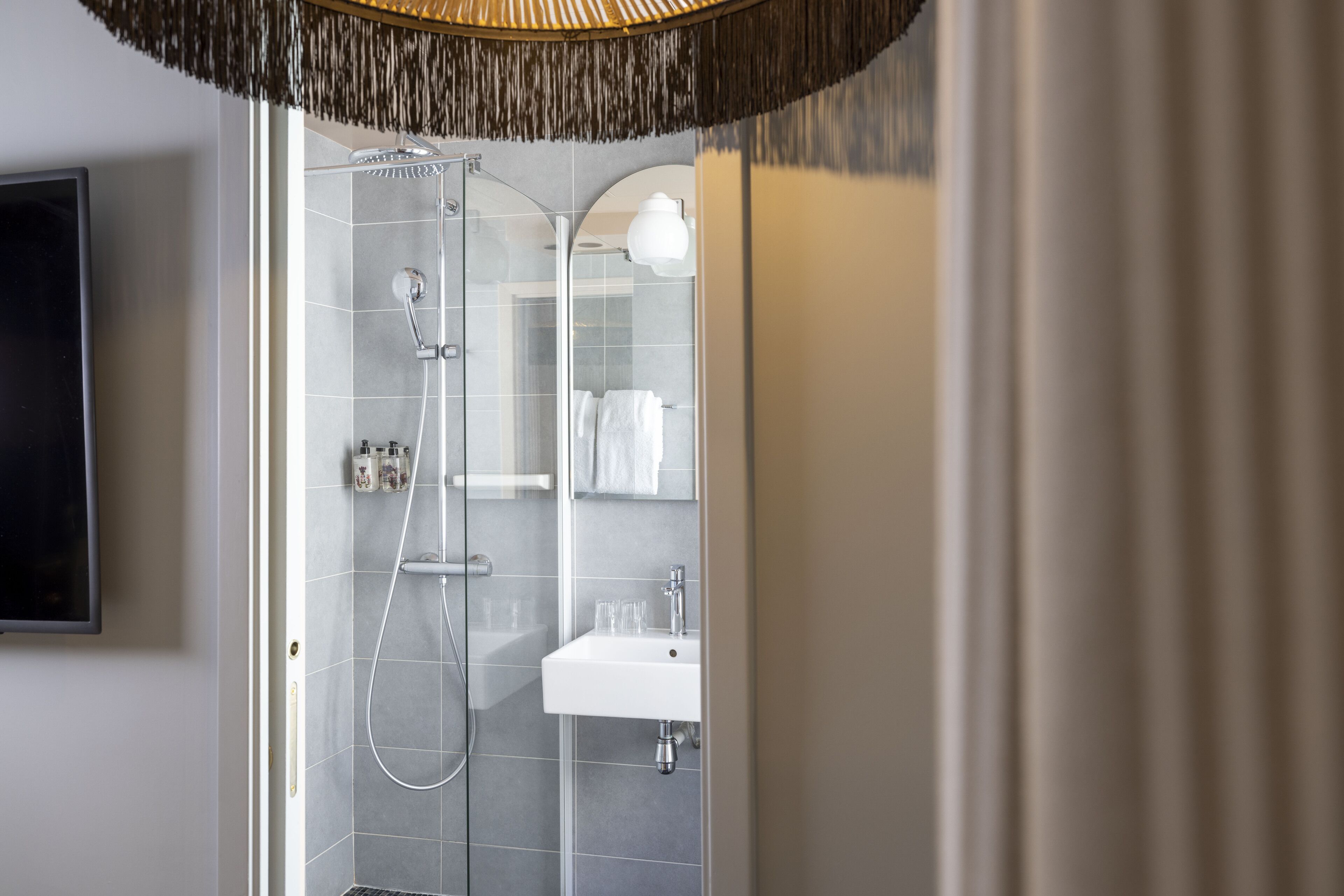 A modern bathroom with a glass-enclosed shower, a white sink, and a mounted television.