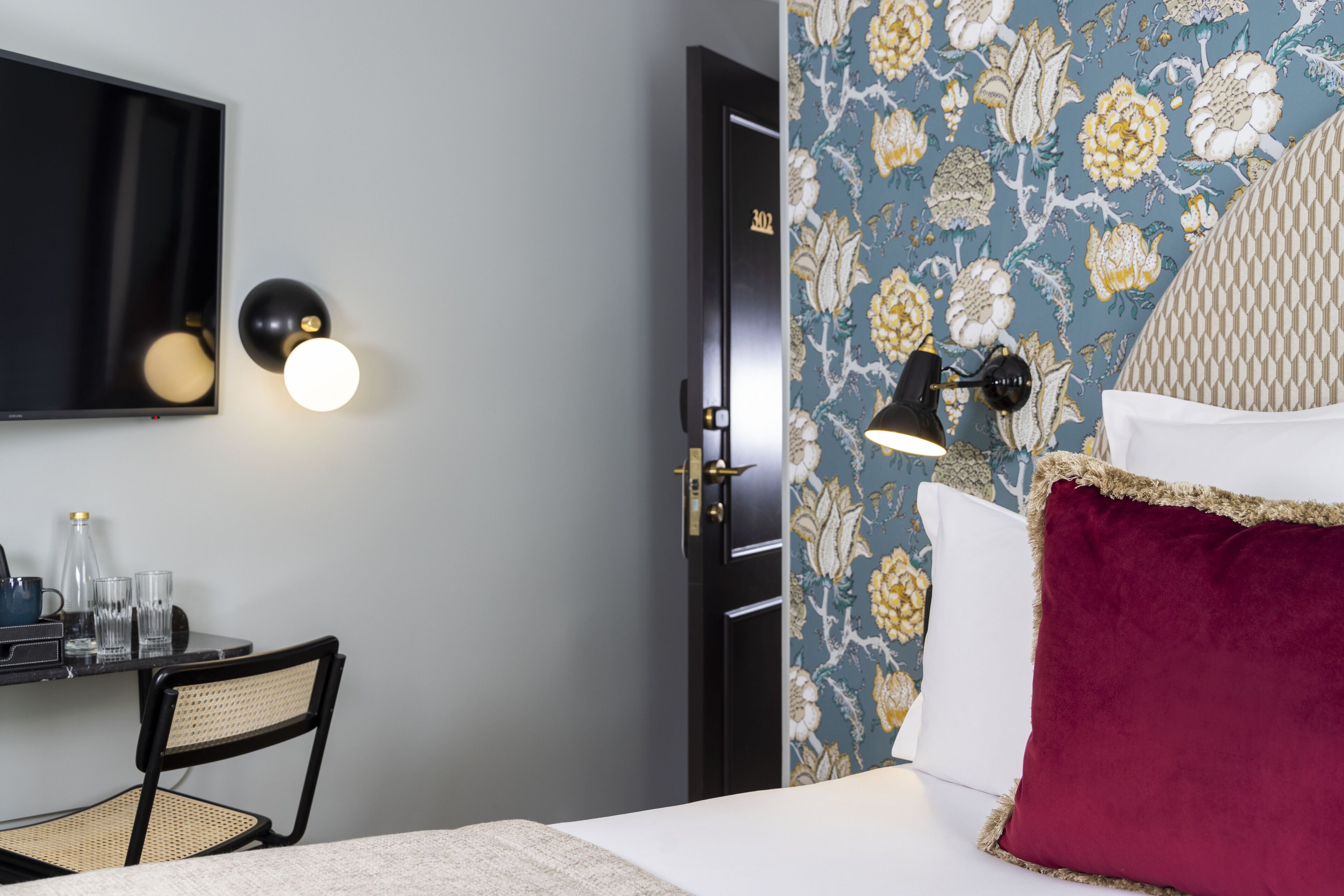 A hotel room with a bed, a desk with a chair, a flat-screen TV, and two wall-mounted lamps.