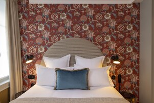 A neatly made bed with white and blue pillows, a patterned floral wallpaper, and two bedside lamps.