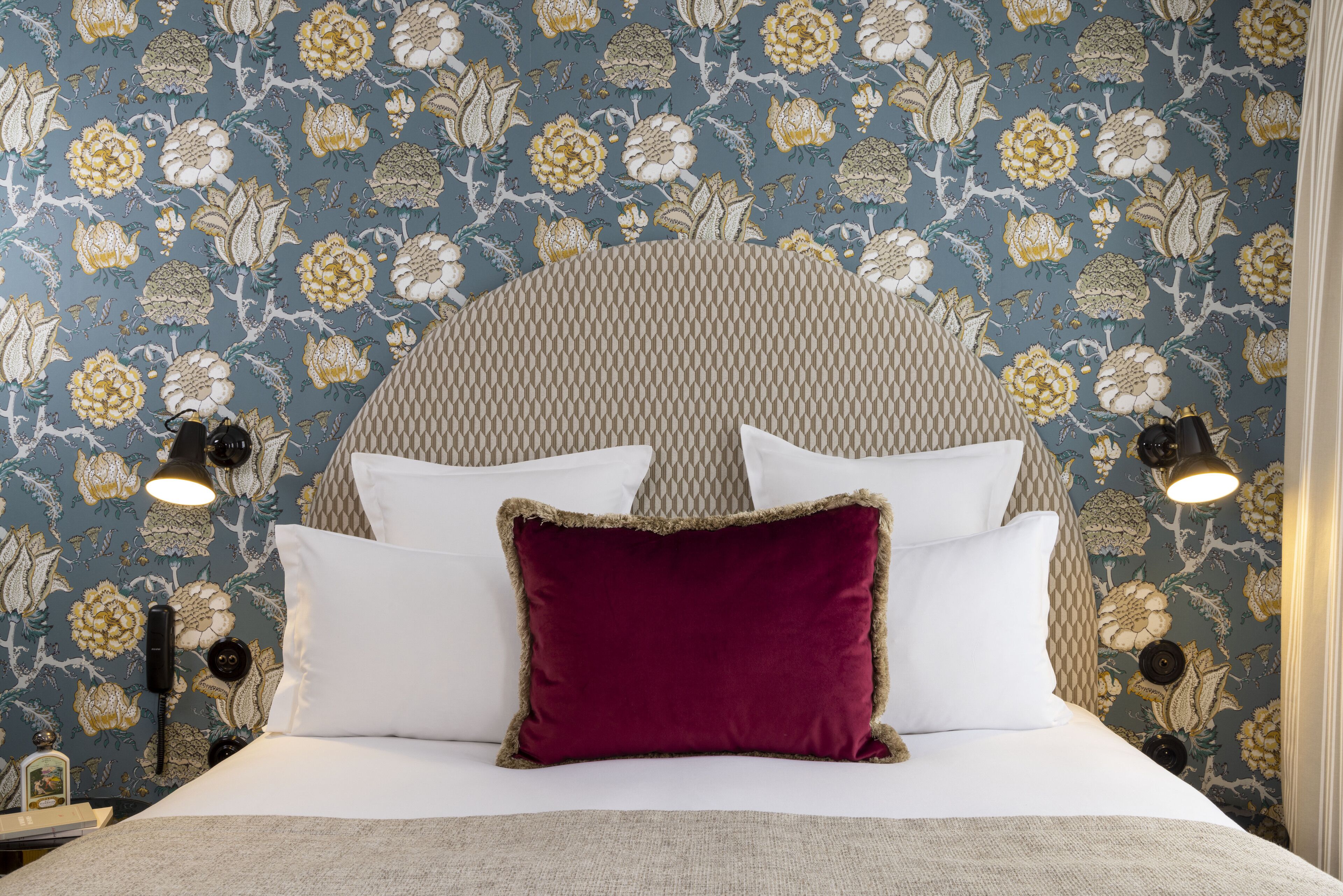 A bed with white and red pillows, a patterned headboard, and wall-mounted lamps.