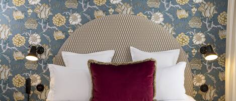 A bed with white and red pillows, a patterned headboard, and wall-mounted lamps.