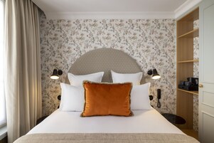A neatly made bed with a headboard, two bedside lamps, and a floral wallpaper.
