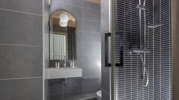 Een moderne badkamer met een wit wastafel, spiegel en douche met een metalen rasterpatroon.