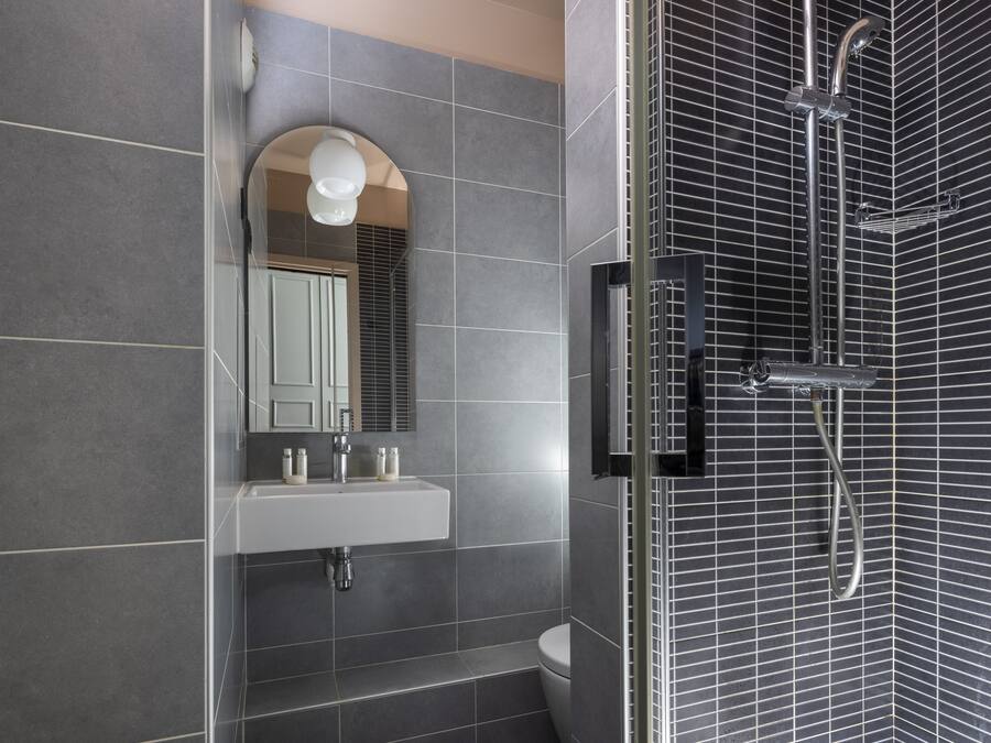 A modern bathroom with a white sink, mirror, and a shower with a metal grid design.