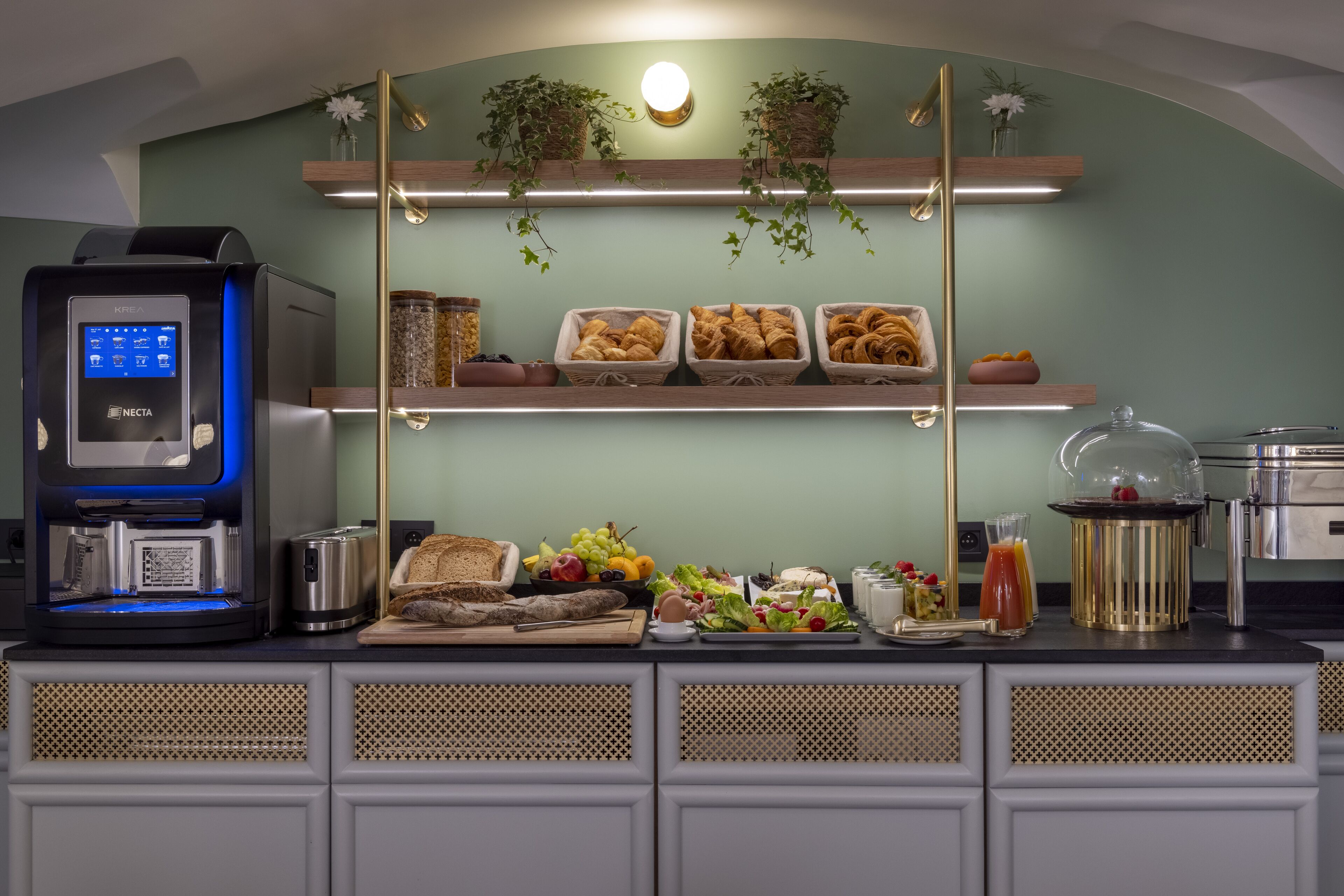 Una barra de desayuno con una máquina de café, pan, frutas y diversas opciones para el desayuno.