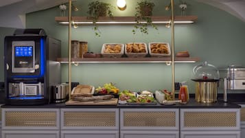 Una barra de desayuno con una máquina de café, pan, frutas y diversas opciones para el desayuno.