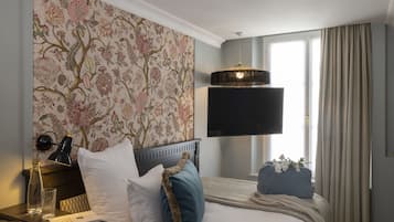 A hotel room with a bed, a flat-screen TV, a desk with a lamp, and a window with curtains.