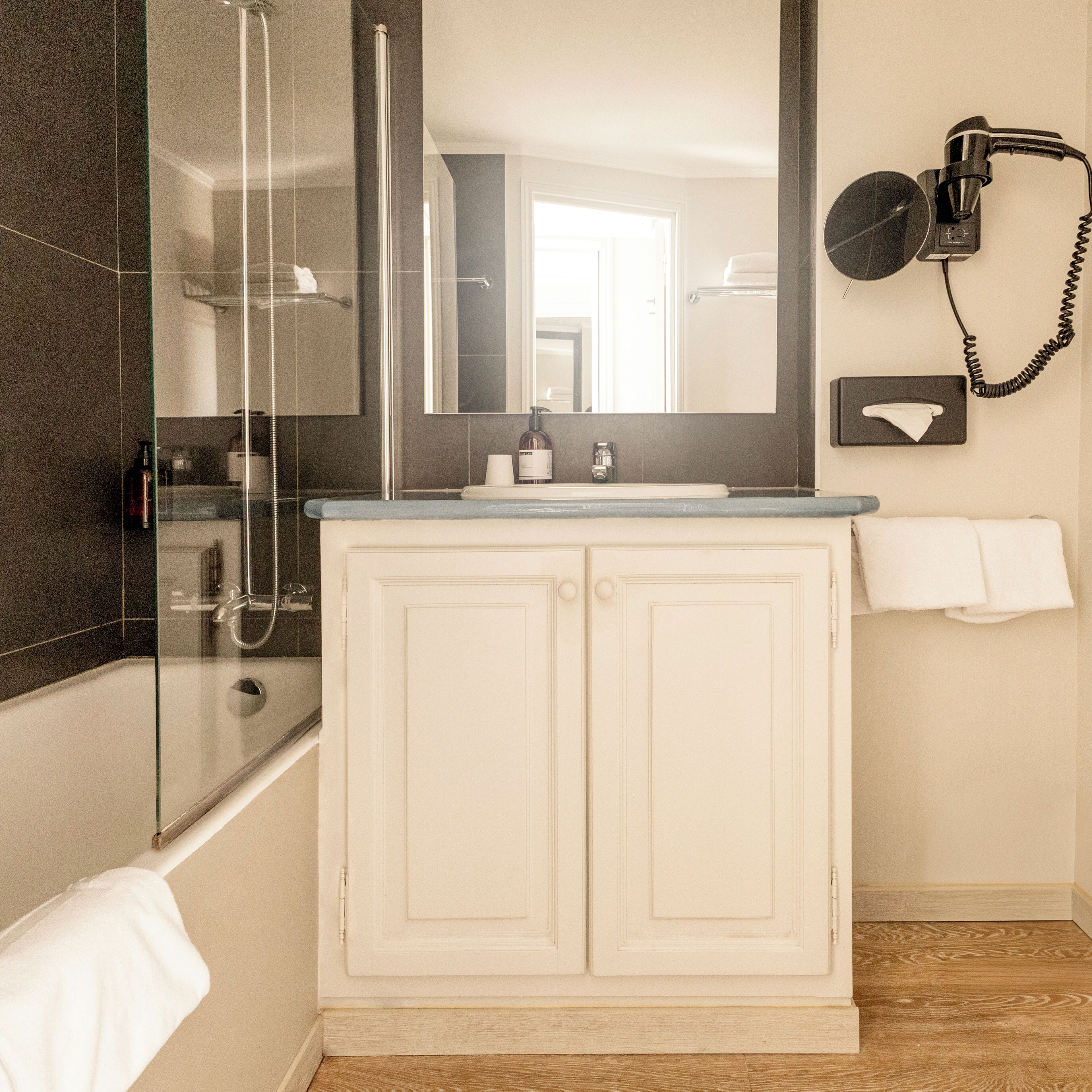 A bathroom with a glass-enclosed shower, a white vanity with a mirror, and a hairdryer mounted on the wall.