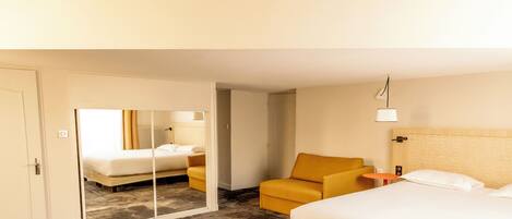 A hotel room with a large bed, a sofa, a small table, and a mirror.
