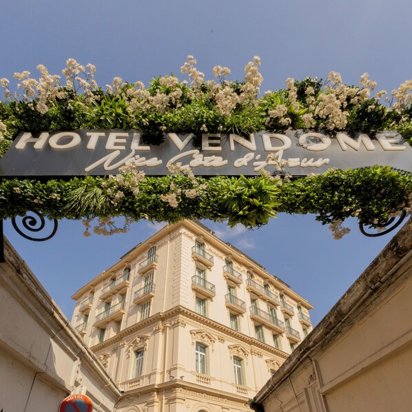 A hotel sign with "HOTEL VENDOME" and "Nice Côte d'Azur" written on it, surrounded by greenery.