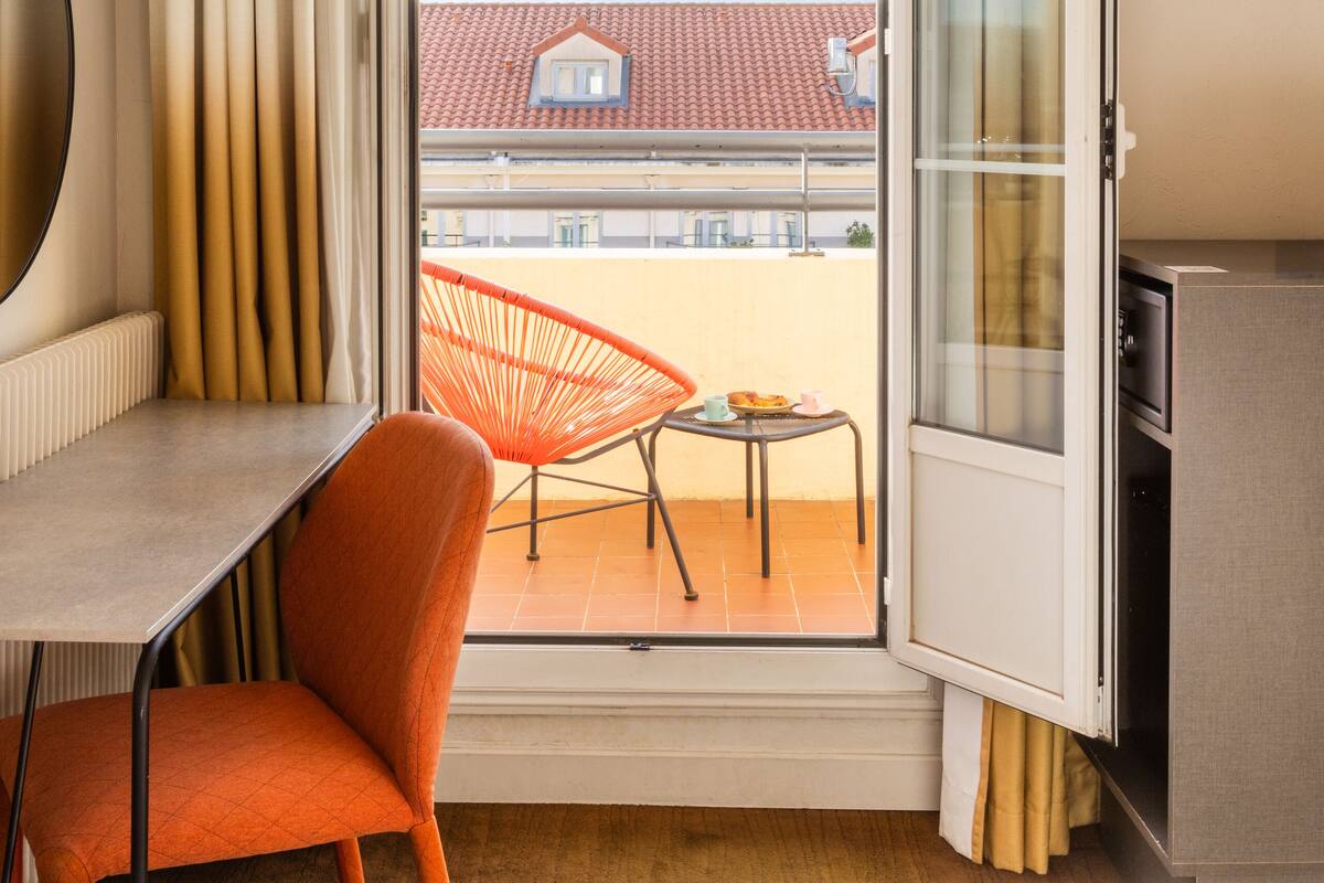 Ein Hotelzimmer mit Balkon, Schreibtisch, Stuhl und Fernseher.