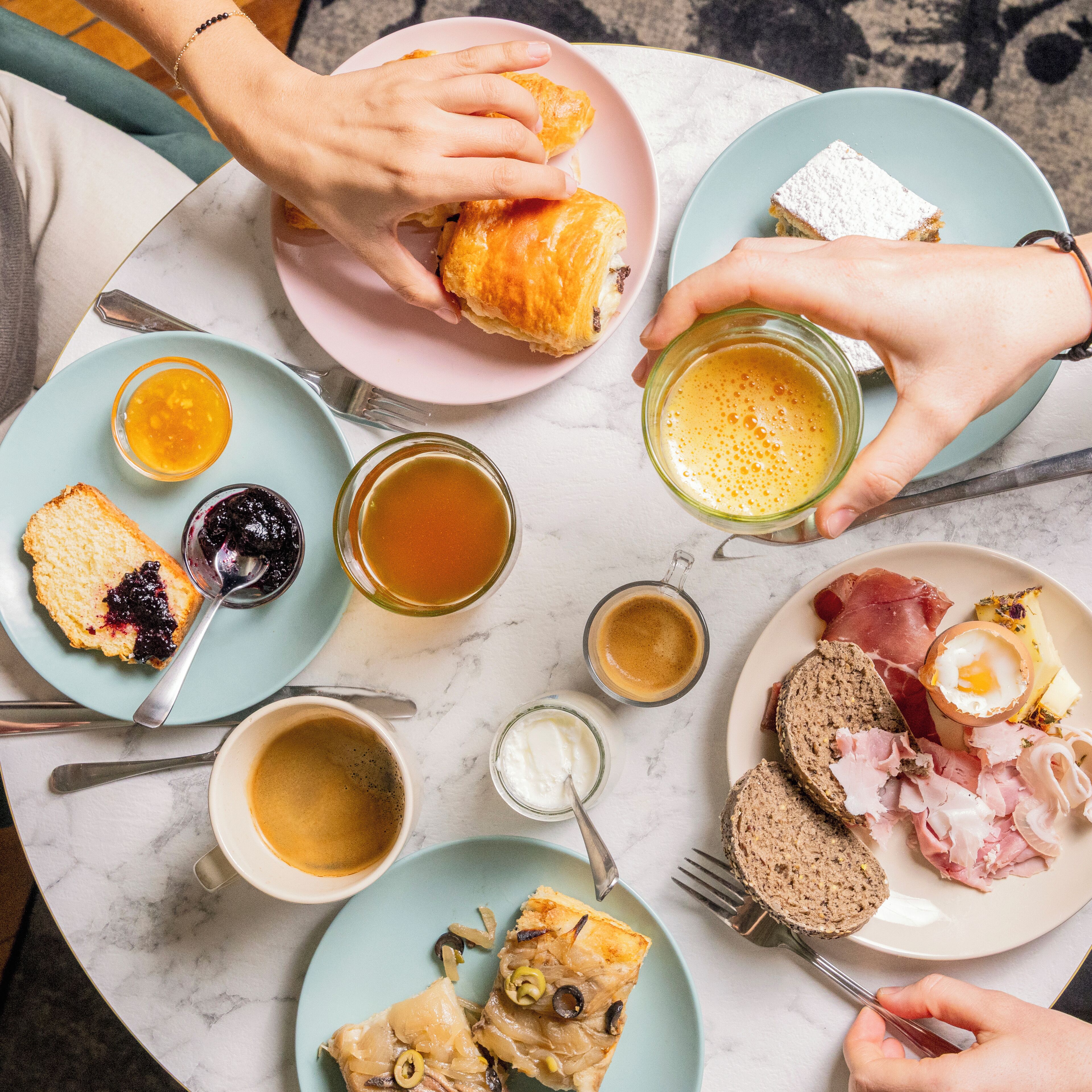 Una mesa con diversos productos para el desayuno, como pasteles, pan, queso y embutidos.