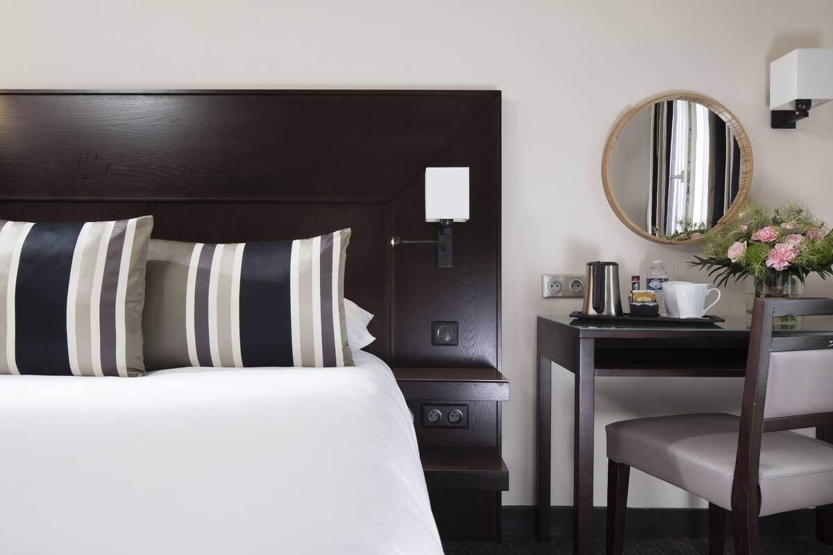 Une chambre d’hôtel avec un lit, une table de chevet, une chaise et un miroir.