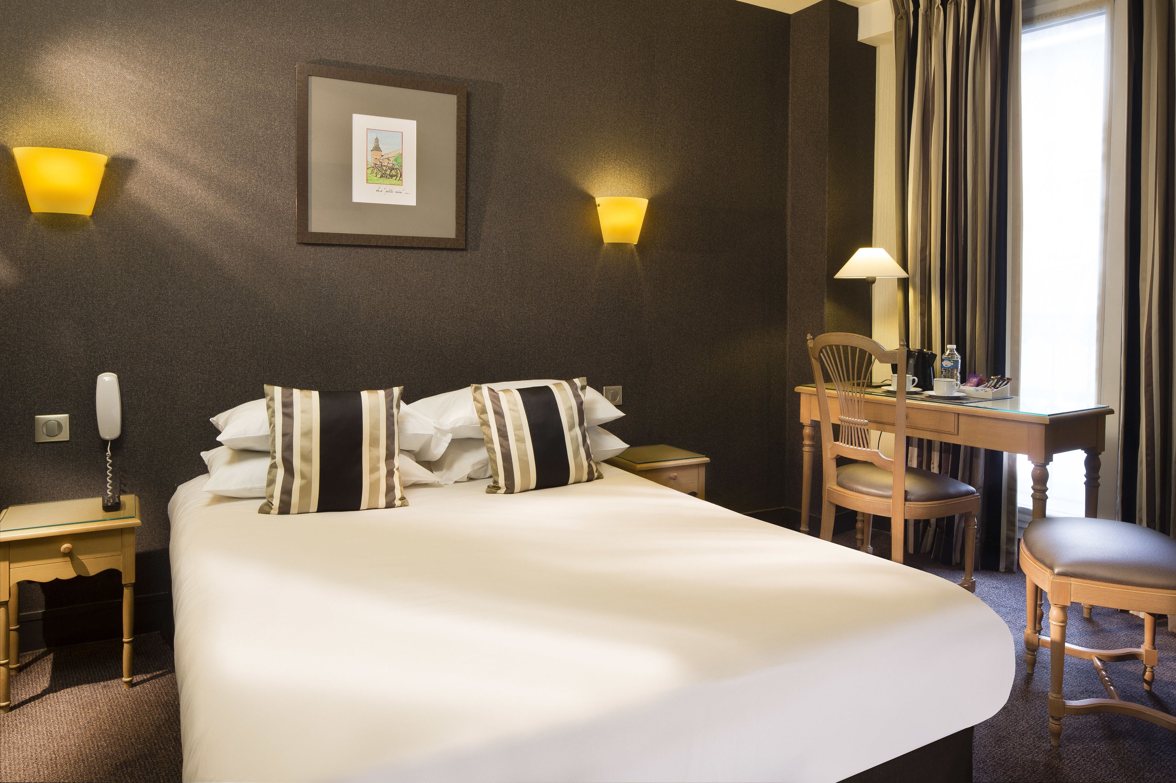 Une chambre d’hôtel avec un grand lit, des tables de chevet, un bureau avec une chaise et deux lampes fixées au mur.