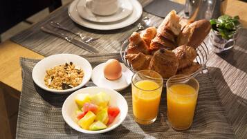 Une table dressée pour le petit-déjeuner, avec des croissants, des fruits, du jus d’orange et une tasse de café.