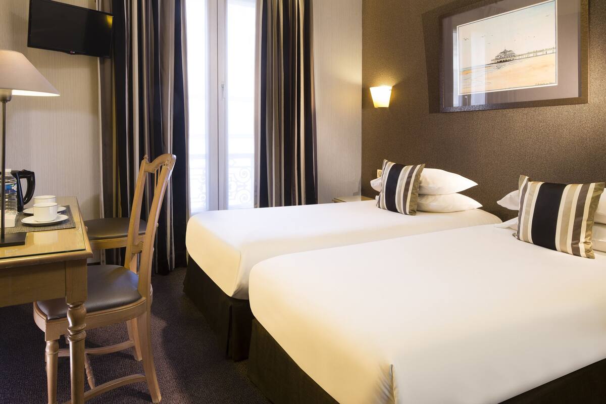Une chambre d’hôtel avec deux lits, un bureau avec une chaise, un téléviseur à écran plat et un tableau au mur.