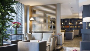 A modern hotel lobby with a seating area, a bookshelf, and a potted plant. - Hotel Albert 1er Paris Lafayette (Paris)