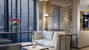 A modern hotel lobby with a sofa, a coffee table, and a vase of flowers. - Hotel Albert 1er Paris Lafayette (Paris)