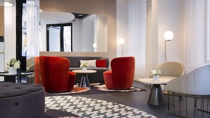 A modern hotel lobby with a sofa, red chairs, a round ottoman, and a patterned rug. - Hôtel Pastel Paris (Paris)