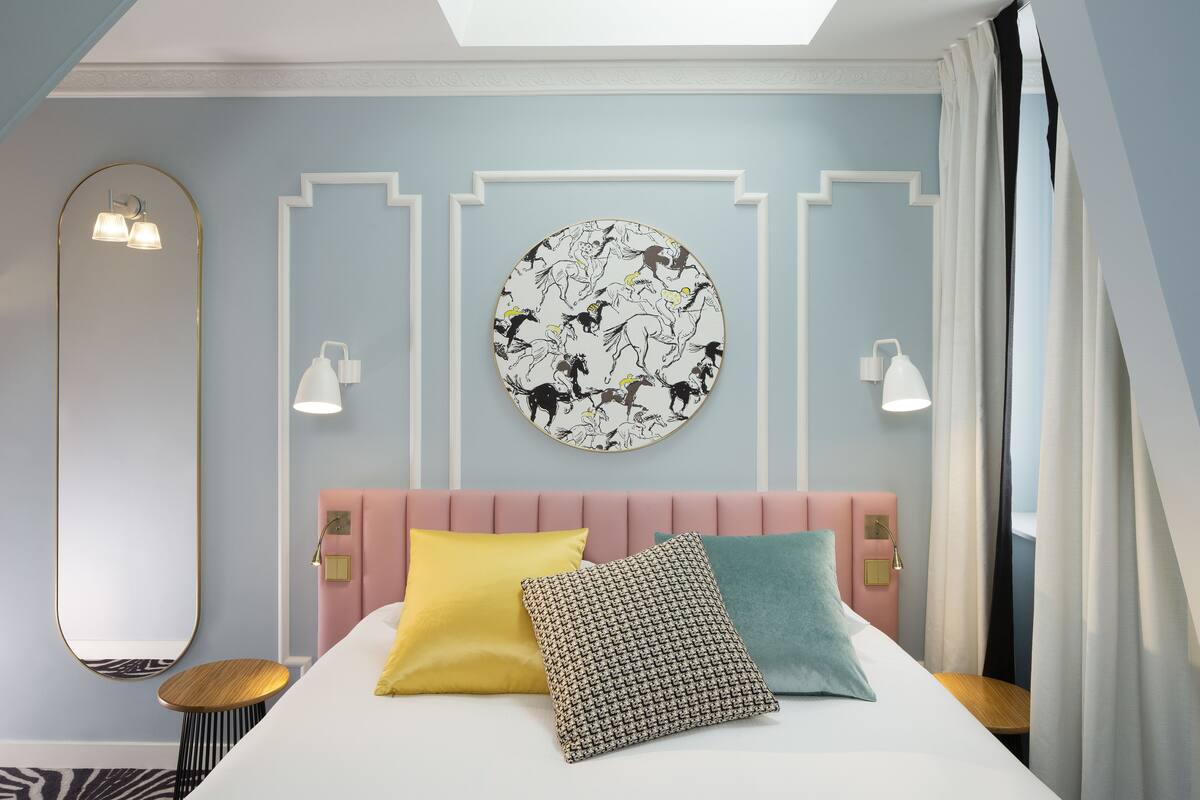 A modern hotel room with a bed, a round wall art piece, a mirror, and a bedside table.