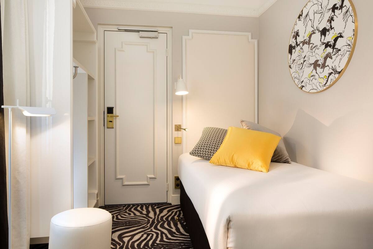 A hotel room with a bed, a zebra-patterned rug, a white door, and a wall art piece.