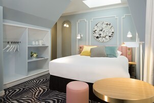 A modern bedroom with a bed, a round wooden table, a zebra-patterned rug, and a wardrobe with hanging clothes.