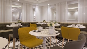 A modern hotel lobby with a checkered floor, a central seating area with a sofa and yellow chairs, and round tables with white tableware. - Hôtel Pastel Paris (Paris)