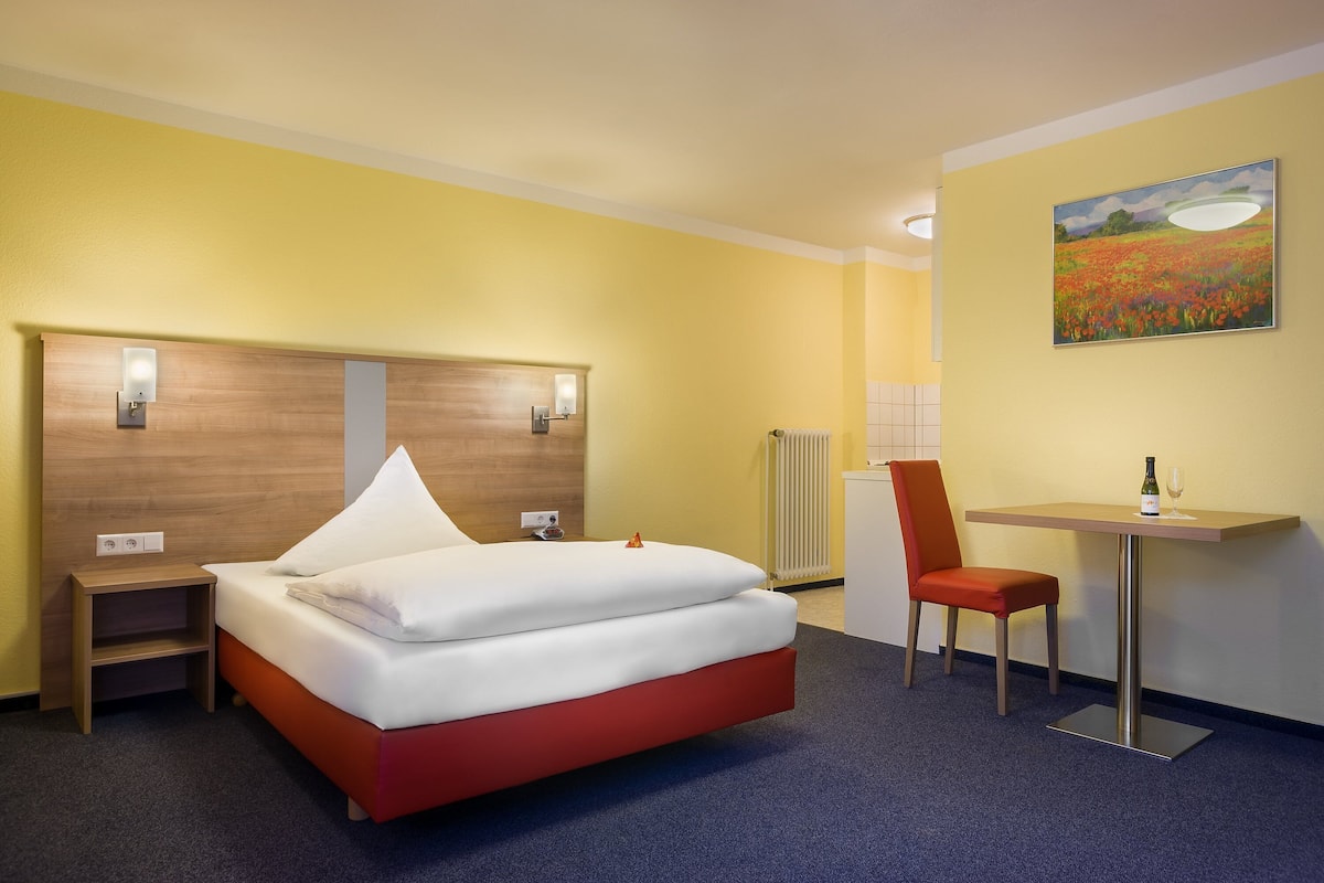 Habitación de hotel con una cama, un escritorio, una silla y un cuadro en la pared.