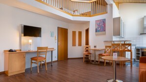 Un interior moderno con un escritorio de madera, sillas, una mesa redonda y una escalera que sube a un nivel superior.