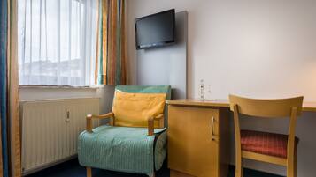 A room with a bed, a desk, a chair, a television, and a window with curtains.