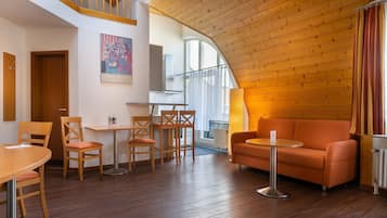 A cozy interior with a wooden ceiling, a sofa, a dining table with chairs, and a kitchen area in the background.
