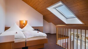Un dormitorio con tragaluz, techo de madera y una cama con ropa de cama blanca.