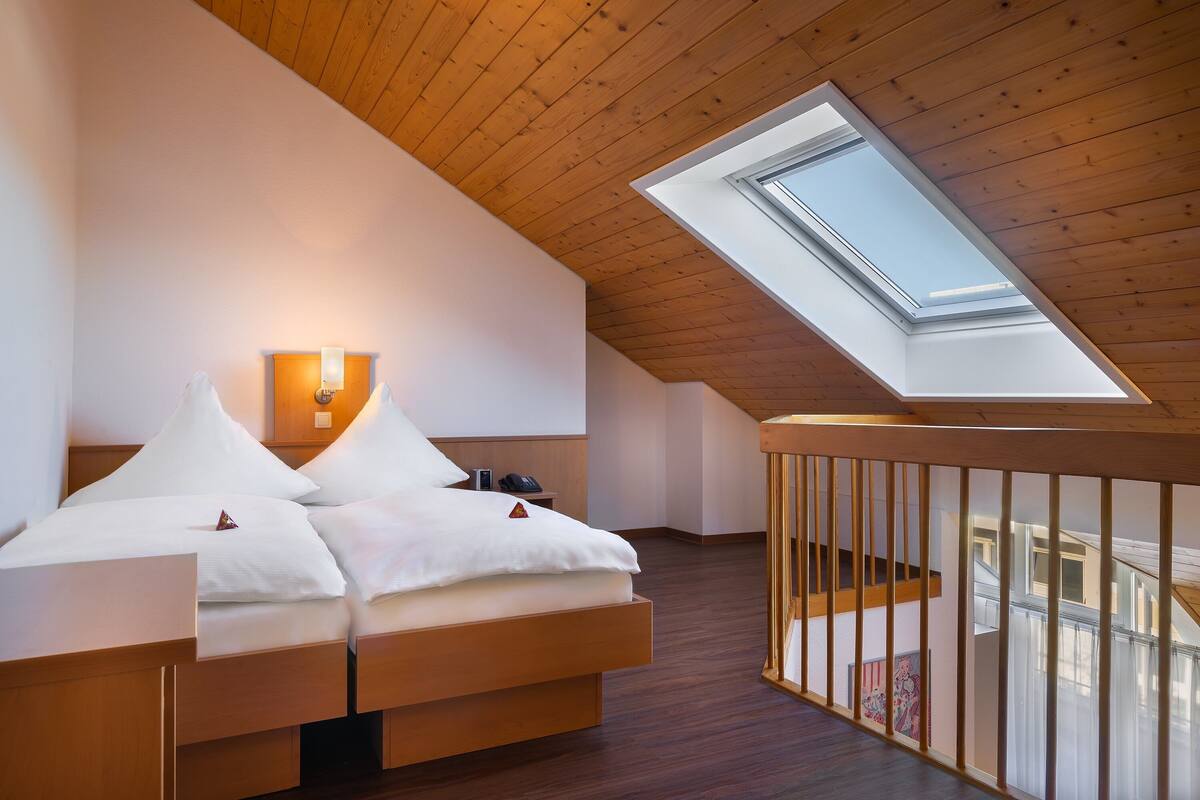 Un dormitorio con tragaluz, techo de madera y una cama con ropa de cama blanca.
