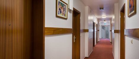 A hotel hallway with wooden doors, a red carpet, and framed artwork on the walls.