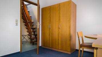 A room with a wooden wardrobe, a dining table with a chair, and a staircase.