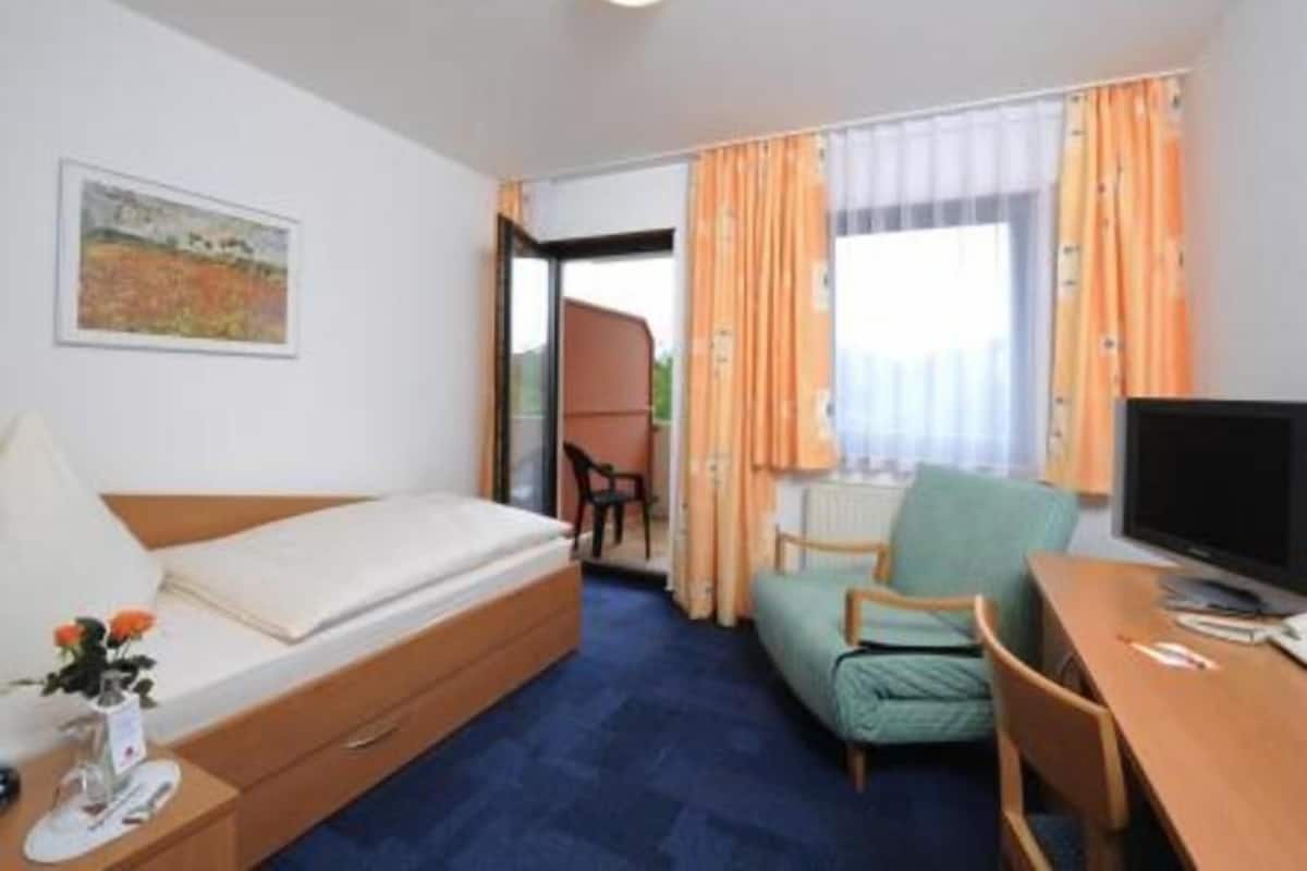 Una habitación con cama, escritorio, silla, televisor y ventana con cortinas.