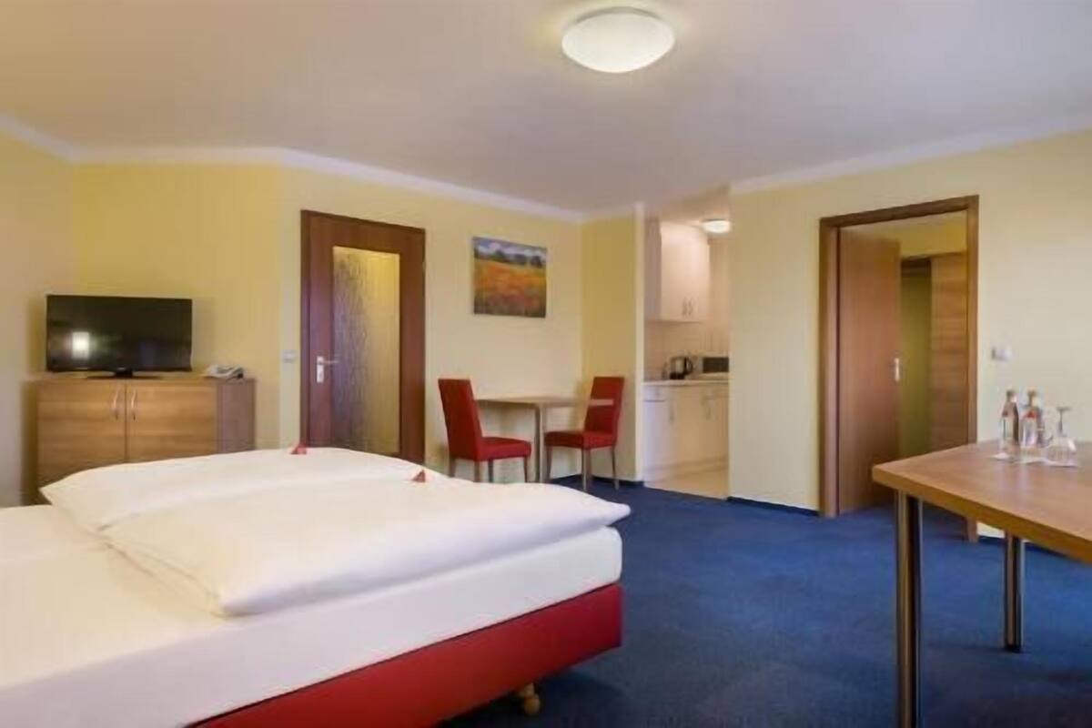Una habitación de hotel con cama, televisión, escritorio y kitchenette.