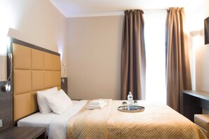 Habitación de hotel con cama, mesita de noche, televisor montado en la pared y ventana con cortinas.
