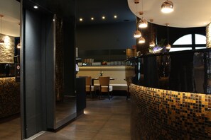 A modern restaurant interior with a dark color scheme, a tiled backsplash, and pendant lighting. - Hotel Delta am Potsdamer Platz (Berlin)